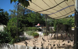 An outdoor patio area with a covered seating area, potted plants, and a view of a building in the background.