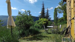 A patio with outdoor furniture, a yellow wall, and a view of trees and hills.