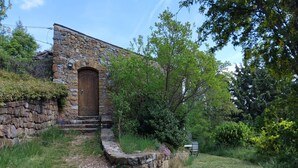 A stone building with a wooden door, surrounded by greenery and trees.