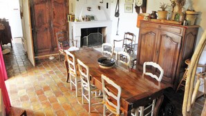 A rustic dining room with a large wooden table, white chairs, a fireplace, and a tiled floor.