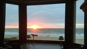 Une pièce avec vue sur l’océan au coucher du soleil, une table et deux chaises.