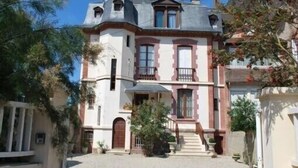 Un bâtiment à deux étages doté d’une façade symétrique, d’une entrée centrale avec des marches et d’un petit balcon au deuxième étage.
