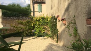 A courtyard with a gravel path, a table with chairs, and a wall with climbing plants and a hanging flower pot. - Holiday house in Provence (Lauris)