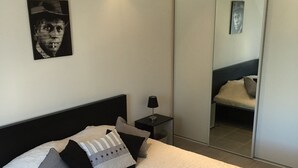 A bedroom with a bed, pillows, a nightstand, a lamp, and a mirror. - Holiday house in Provence (Lauris)