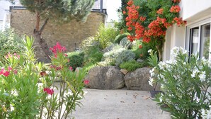 A garden with various plants and flowers, a stone wall, and a building with a window.