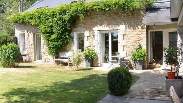 A stone house with a garden, a wooden deck, and a patio area with outdoor furniture.