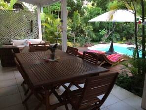 Ett träbord med stolar, en soffa av rotting och en pool i bakgrunden.
