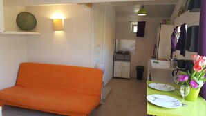 Un espace de vie compact comprenant un canapé, une table à manger avec des assiettes et un verre, et une petite cuisine en arrière-plan.