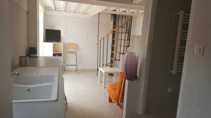 Une chambre d’hôtel compacte avec une baignoire blanche, un petit bureau avec une télévision, une chaise et un escalier doté d’une rampe en bois.
