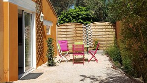 Une maison avec une terrasse en gravier, une clôture en bois et des chaises colorées.