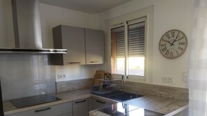 A modern kitchen with a built-in stove, a sink, and a window with blinds. - Appt Leucate- La Franqui.  3 rooms, beach at 50 m, Terrace, free Wifi, (Leucate)