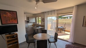 A modern kitchen with a dining area, a TV, and a ceiling fan. - Appt Leucate- La Franqui.  3 rooms, beach at 50 m, Terrace, free Wifi, (Leucate)