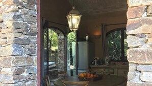 Un coin repas aux murs de pierre, avec une table ronde, quatre chaises et un luminaire suspendu.