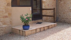 Un edificio de piedra con techo de tejas, una puerta con ventanal y una planta en maceta sobre una pequeña plataforma.