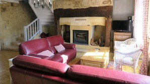 Una sala de estar con un sofá de cuero rojo, un sillón de mimbre blanco, una chimenea y un televisor.