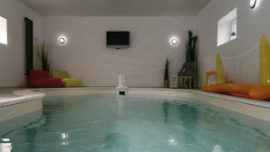 Una piscina con una pequeña estatua en el centro, rodeada de sillas de descanso amarillas y anaranjadas.