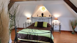 Un dormitorio acogedor en el ático, con techo inclinado, estructura de cama metálica, dos mesitas de noche con lámparas y una pequeña estantería decorativa.