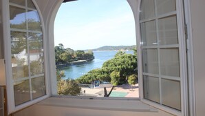 A view from a room with an arched window overlooking a body of water, trees, and a distant shoreline. - Magnificent Lake View, Hossegor City Center, 10 min walk to the Ocean, Large Terrace (Soorts-Hossegor)