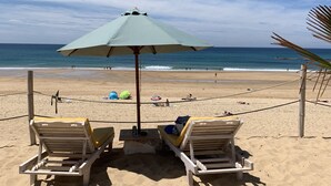 A beach with two wooden lounge chairs, a table, and a green umbrella. - Magnificent Lake View, Hossegor City Center, 10 min walk to the Ocean, Large Terrace (Soorts-Hossegor)