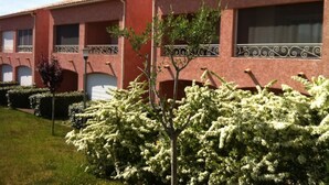 Una hilera de edificios con techos rojos y balcones, rodeada de arbustos cuidados y un pequeño árbol.