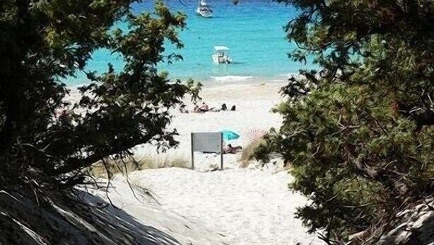 Una playa con agua turquesa cristalina, algunas embarcaciones y una orilla arenosa.