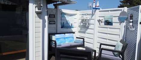 An outdoor deck with a table and two chairs, a white fence, and a sign with the word 'COTE OUEST'.