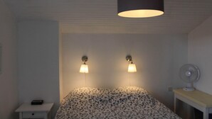 A bedroom with a bed, two wall-mounted lamps, a ceiling fan, and a nightstand with a remote control.
