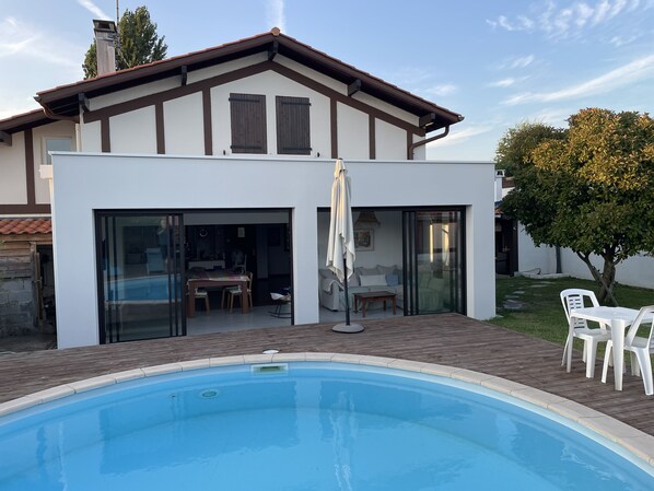 Uma casa moderna com piscina, um pátio com móveis de exterior e uma grande árvore.