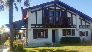 A two-story house with a balcony, a stone foundation, and a well-maintained lawn.