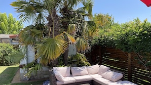 A wicker sofa with cushions, a matching ottoman, and a wooden deck.
