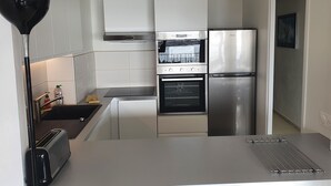 Une cuisine moderne avec des meubles blancs, un four encastré, un réfrigérateur et un grille-pain.
