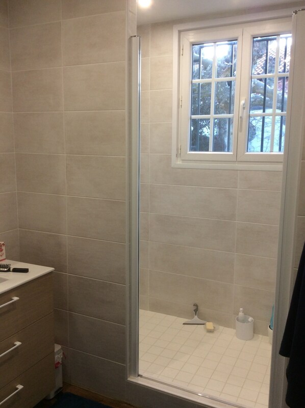 A bathroom with beige tiles, a glass shower enclosure, a window with a view of trees, and a small shelf with toiletries. - Bidart, House 6 - 8 pers, 3*, 100m from surf beaches (Bidart)