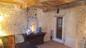 Een rustieke kamer met stenen muren, een houten plafond, een tafel met stoelen, een spiegel en een vaas.