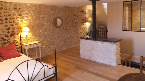 Een slaapkamer met een stenen muur, een bed met metalen frame, een nachtkastje met een lamp, een houten vloer en een klein tafeltje met een stoel.