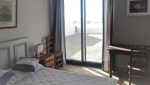 Hotellihuone, jossa on sänky, työpöytä, tuoli ja suuri ikkuna, josta avautuu näkymä rannalle.