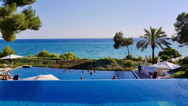 Une piscine à l’eau d’un bleu cristallin, entourée de verdure et offrant une vue sur la mer.
