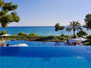 Ein Pool mit klarem, blauem Wasser, umgeben von viel Grün und Blick aufs Meer.