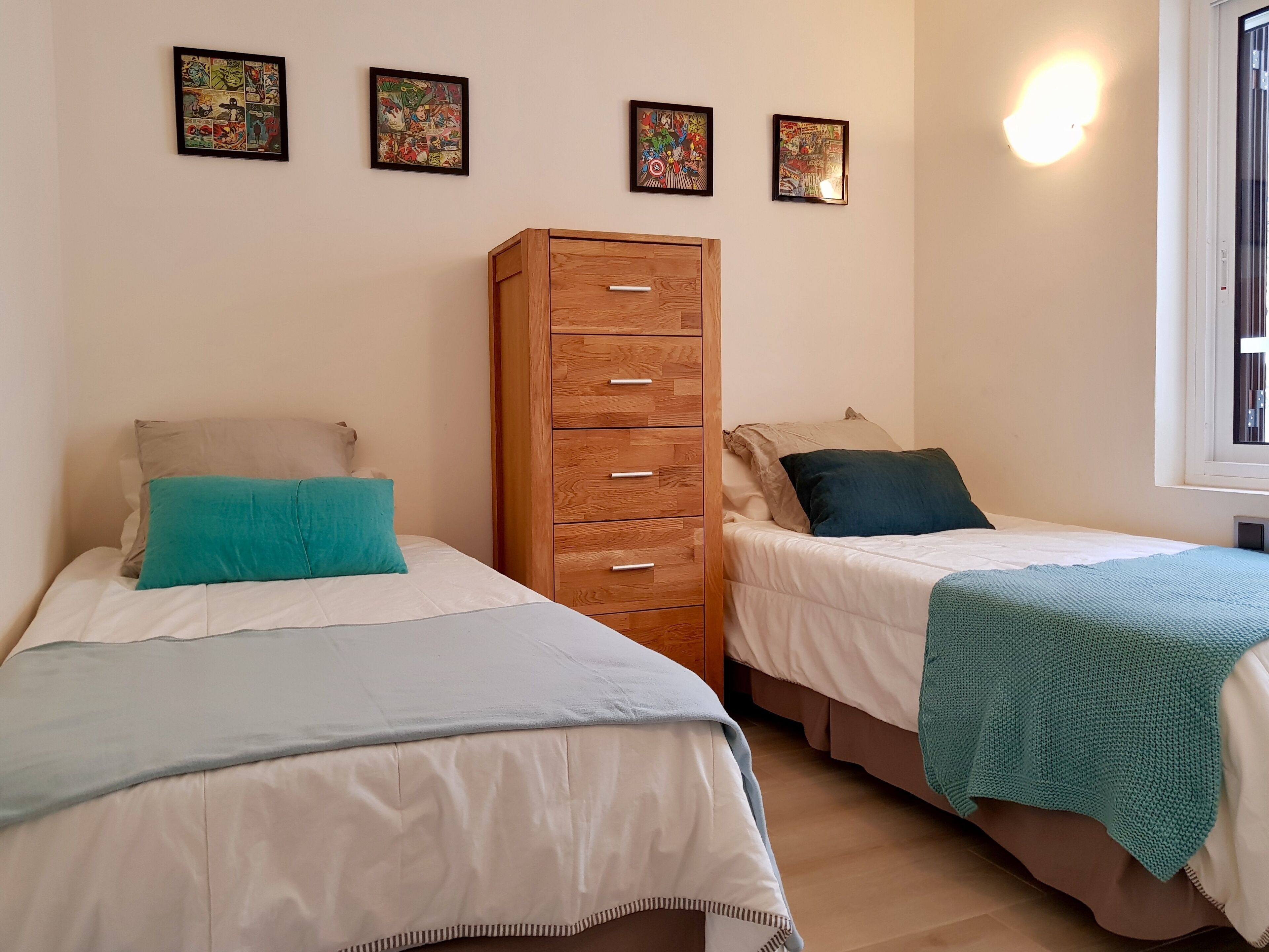Un dormitorio con dos camas, un armario de madera y tres cuadros en la pared.