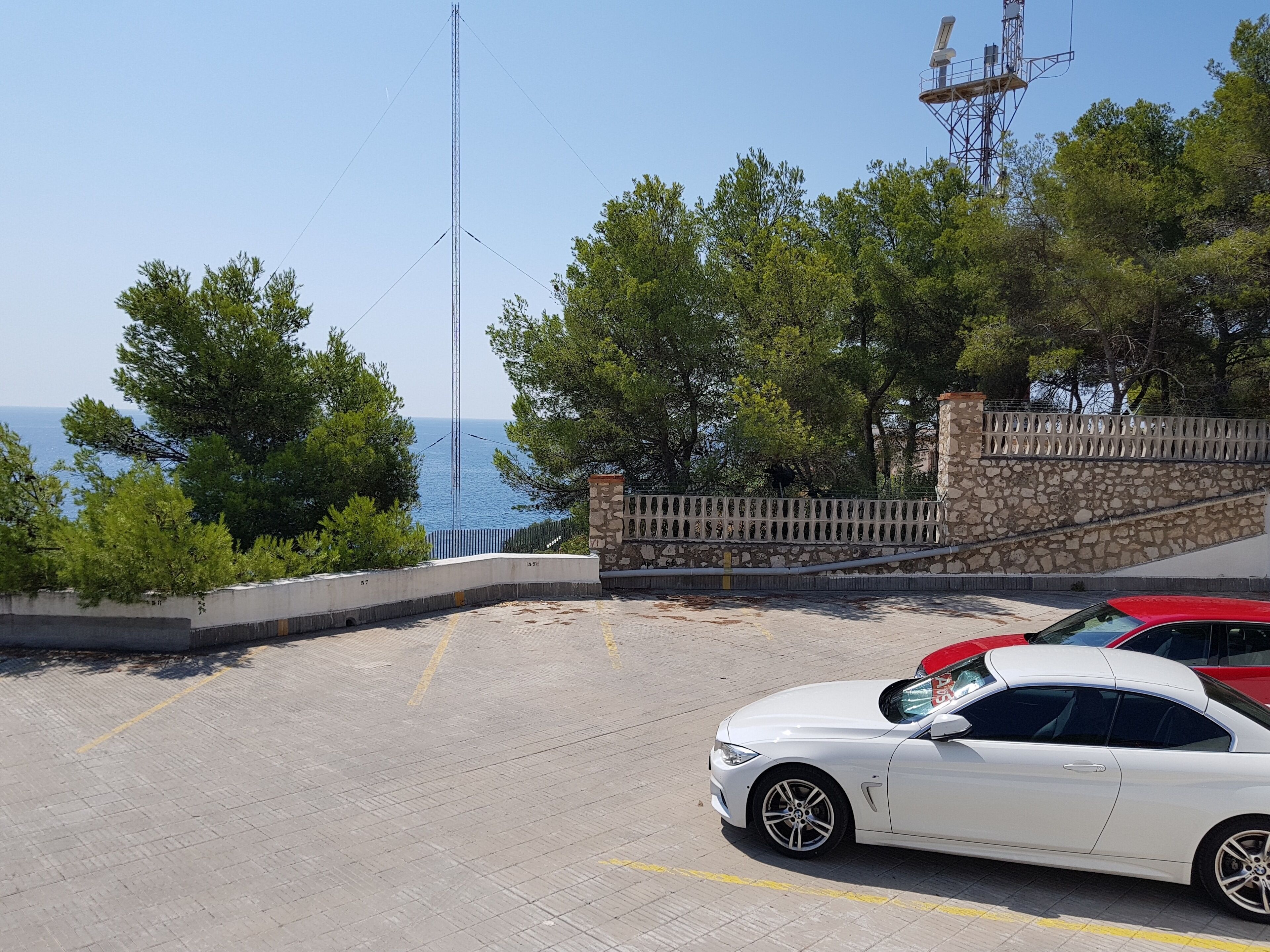 Ein Parkplatz mit einem weißen Auto, einer Steinmauer und Blick auf das Meer.