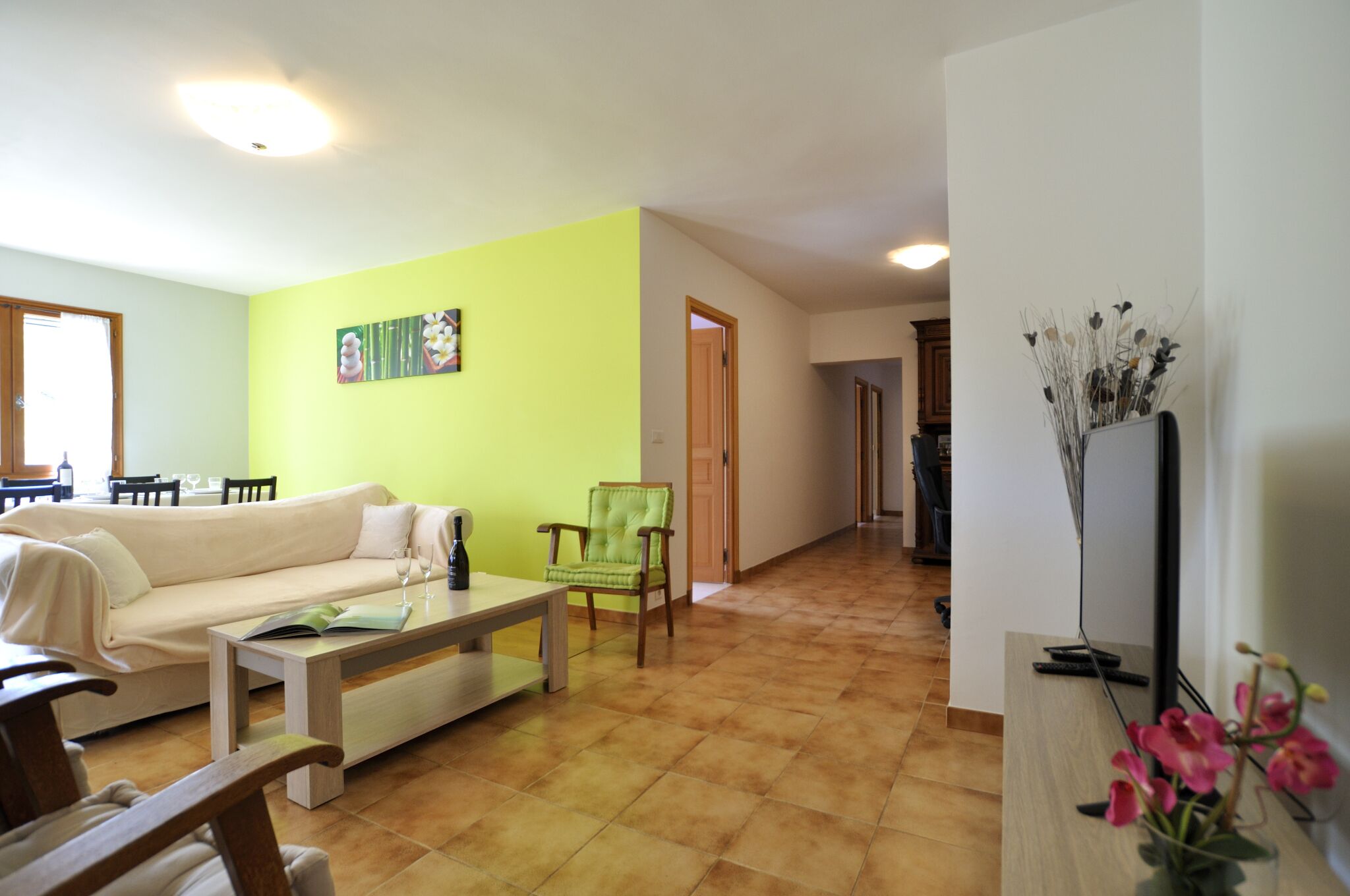 Un salon avec un mur vert, un canapé beige, une table basse en bois et un fauteuil vert.