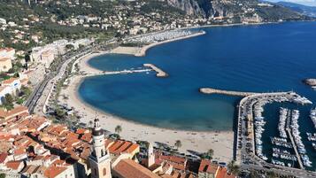 Vista aérea de un pueblo costero con puerto deportivo, playa y edificios residenciales.