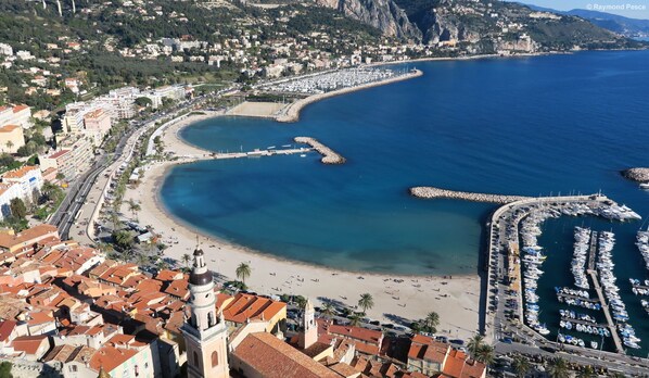 Vue aérienne d’une ville côtière avec un port de plaisance, une plage et des immeubles résidentiels.