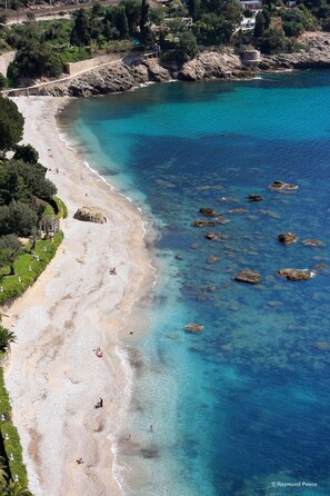 Une plage côtière aux eaux turquoise et limpides, parsemée de rochers et bordée d’une promenade pavée.