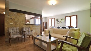 Ein Wohnzimmer mit Steinwand, Holzbalke, beiges Sofa, Couchtisch und zwei Sesseln.