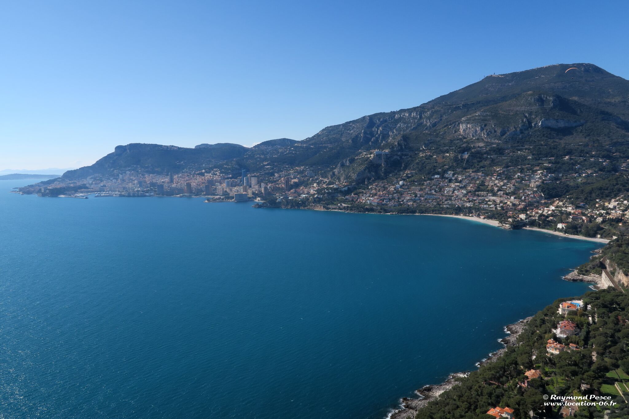 A coastal city with a prominent mountain, clear blue sea, and dense urban development along the coastline.