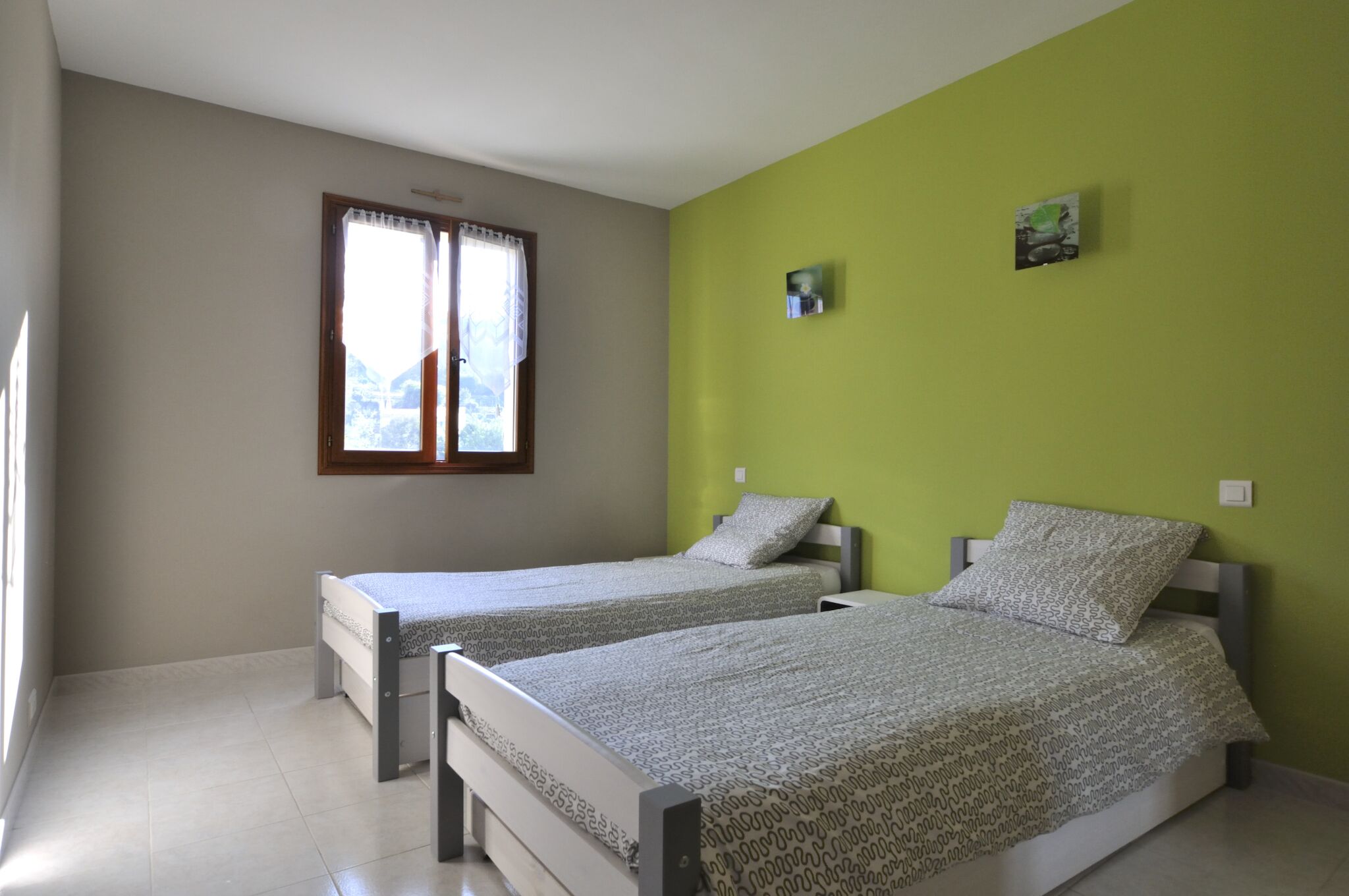 Un dormitori amb dos llits, una finestra amb cortines i una paret verda.