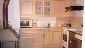 A compact kitchen with wooden cabinets, a microwave, a toaster, and a stove. - Chalet overlooking a pond in a green setting. (Augignac)