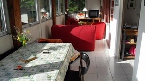 A room with a dining table, red sofa, TV, and a bookshelf. - Chalet overlooking a pond in a green setting. (Augignac)