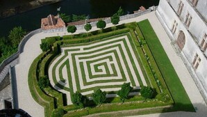 An aerial view of a maze garden with a circular layout, surrounded by a stone wall and a body of water. - Chalet overlooking a pond in a green setting. (Augignac)