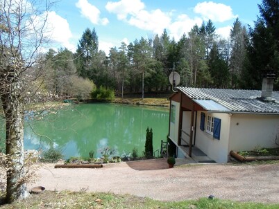 Chalet overlooking a pond in a green setting.